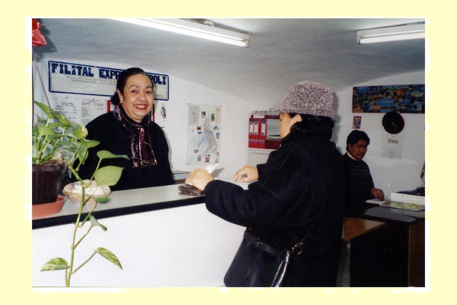 In questa immagine è ritratta una immigrata sorridente, assieme ad una connazionale, mentre svolge le sue attività lavorative presso un’agenzia che a Napoli, agli inizi del nuovo millennio, si occupava di inviare o ricevere denaro fra l’Italia e le Filippine: Filital. foto 1