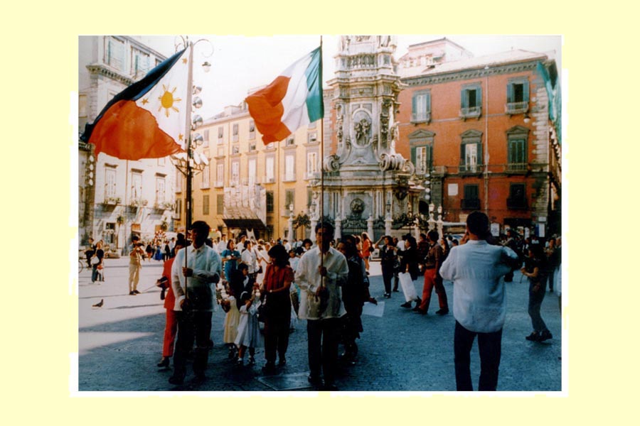Apertura della processione del 19 maggio 1996. Il corteo attraversa la piazza del Gesù Nuovo fra la folla incuriosita di passanti, turisti e residenti del luogo. Proseguirà, poi, fino alla chiesa per terminare con l’offerta alla Vergine Maria. Gli uomini sono, qui, vestiti con la camicia tradizionale, “barong tagaolg” e portano sia la bandiera italiana, che quella filippina, quale simbolo della loro, oramai, duplice appartenenza. foto 1
