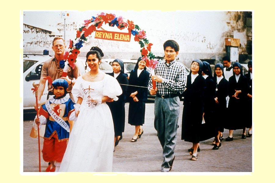 La regina Elena è il personaggio principale di Santacruzan. In questa foto che fa riferimento alla processione del 19 maggio del 1996, porta fra le mani una piccola croce, emblema del ritrovamento di quella sacra sulla quale Gesù morì ed è accompagnata da Costantino, suo figlio. Da questa immagine si evince come nel corso di queste celebrazioni i bambini possano essere coinvolti in processi di inculturazione religiosa o legata alle tradizioni nelle Filippine. A questa processione, inoltre, presero parte anche alcune suore di origine filippina residenti a Napoli. foto 1